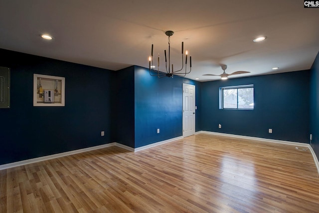 empty room with ceiling fan with notable chandelier, light wood finished floors, recessed lighting, and baseboards