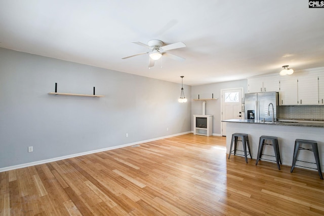 kitchen with white cabinets, decorative backsplash, light wood-style flooring, a kitchen bar, and stainless steel refrigerator with ice dispenser