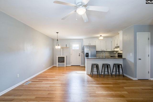 kitchen with a peninsula, visible vents, white cabinets, light wood-type flooring, and stainless steel fridge with ice dispenser