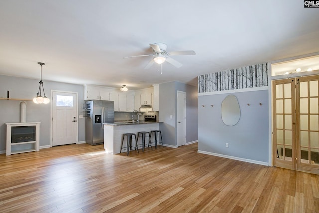 unfurnished living room featuring a sink, light wood-style floors, baseboards, and a ceiling fan