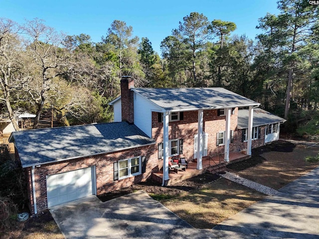 view of front of house featuring a garage, driveway, a chimney, a porch, and brick siding