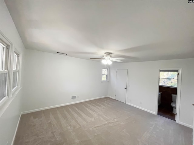 unfurnished bedroom featuring visible vents, light carpet, ceiling fan, ensuite bath, and baseboards