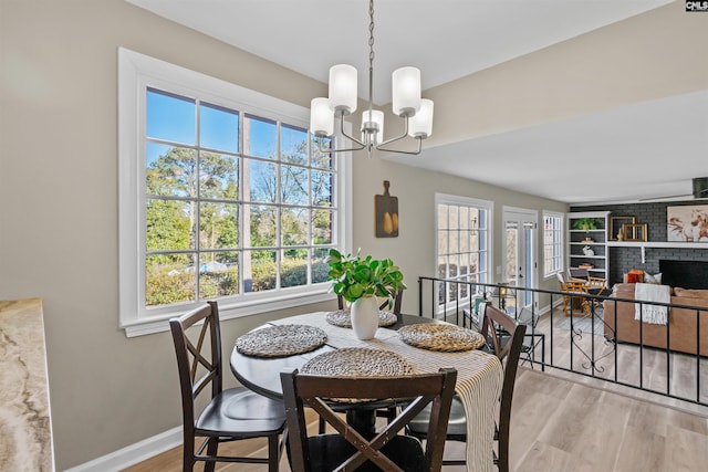 dining space with a brick fireplace, a notable chandelier, baseboards, and wood finished floors