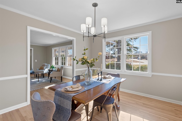 dining area with light wood-type flooring, baseboards, ornamental molding, and a notable chandelier