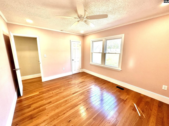 empty room featuring hardwood / wood-style flooring, visible vents, a ceiling fan, baseboards, and ornamental molding