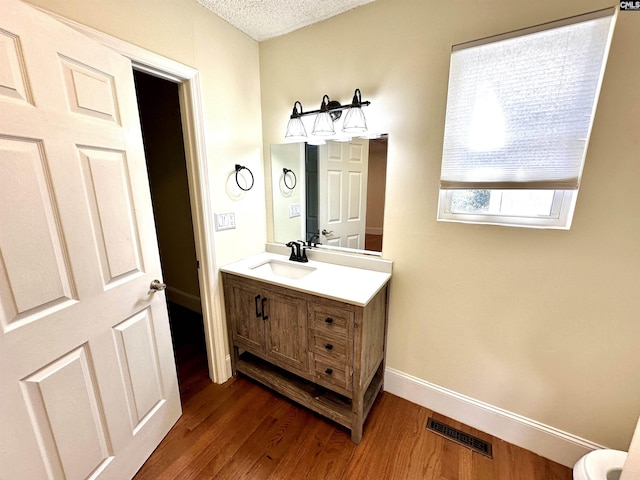 bathroom with a textured ceiling, wood finished floors, vanity, visible vents, and baseboards