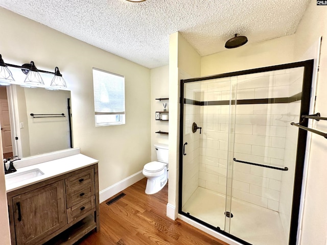 bathroom with toilet, a shower stall, visible vents, and wood finished floors