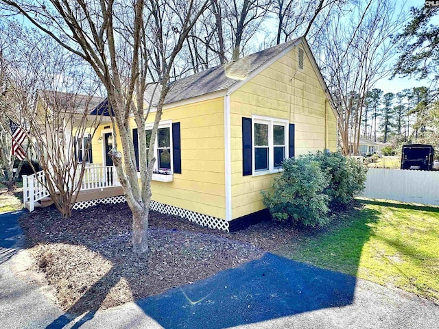 view of home's exterior featuring covered porch, a shingled roof, and fence