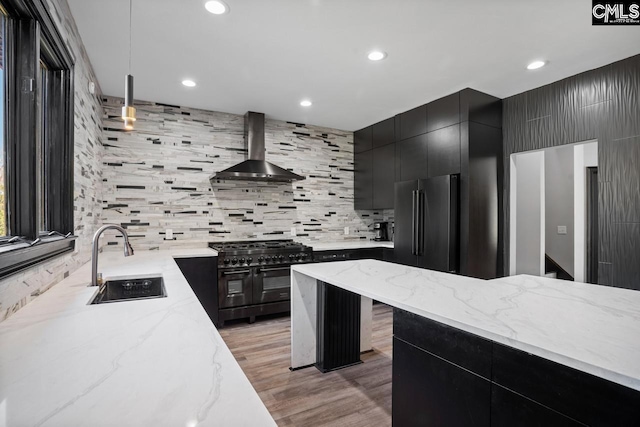 kitchen featuring decorative backsplash, high end appliances, dark cabinets, wall chimney range hood, and a sink