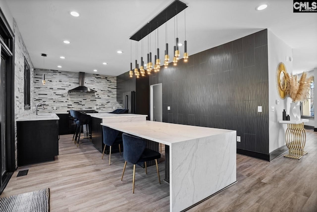 kitchen with high end refrigerator, a spacious island, light wood-type flooring, wall chimney range hood, and a sink