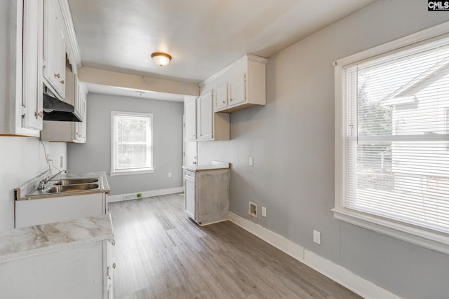 kitchen with light wood finished floors, baseboards, under cabinet range hood, white cabinetry, and a sink