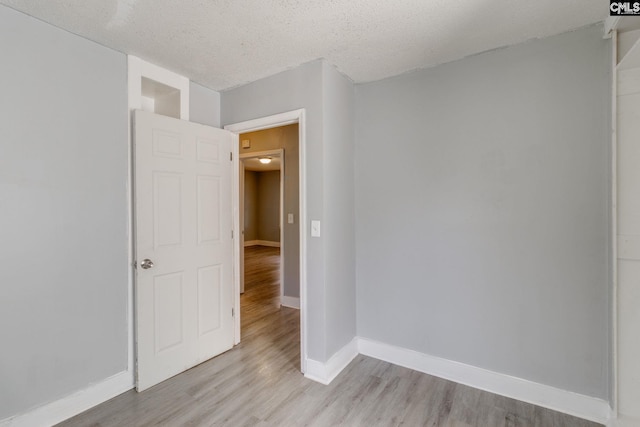 empty room with light wood finished floors, baseboards, and a textured ceiling