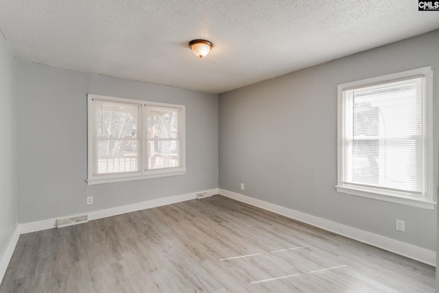 spare room featuring a textured ceiling, wood finished floors, visible vents, and baseboards