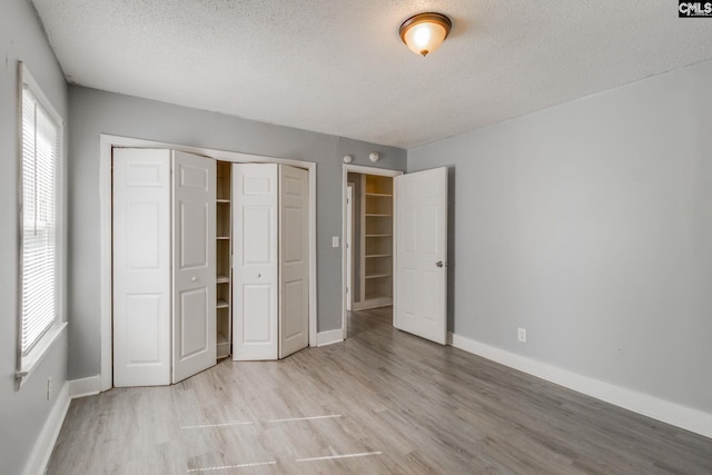 unfurnished bedroom with a closet, baseboards, a textured ceiling, and light wood finished floors