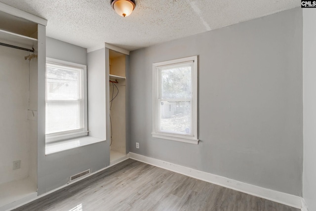 interior space with baseboards, a textured ceiling, visible vents, and wood finished floors