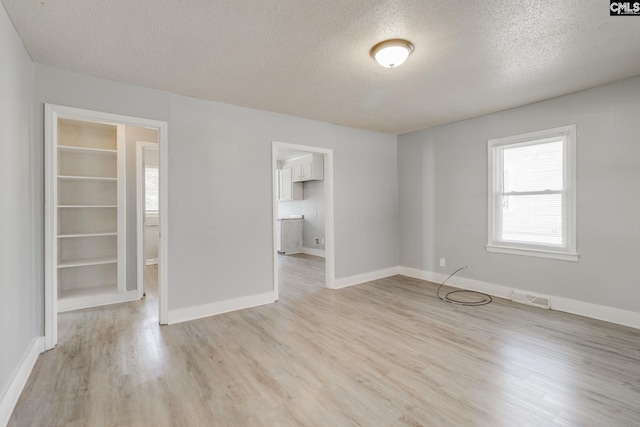 empty room with light wood-style floors, visible vents, a textured ceiling, and baseboards