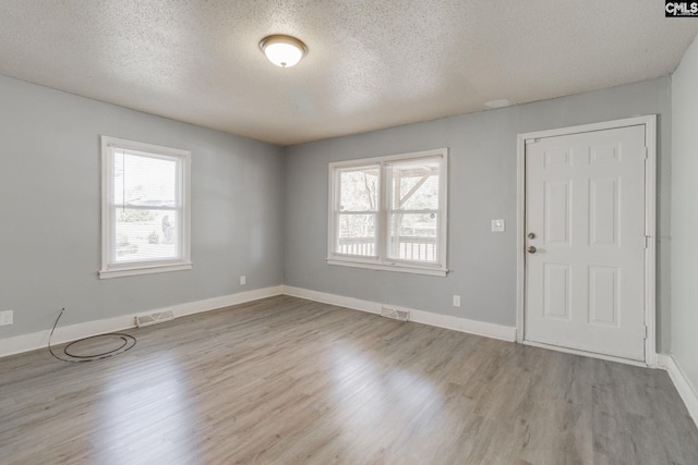 unfurnished room featuring baseboards, a textured ceiling, visible vents, and wood finished floors