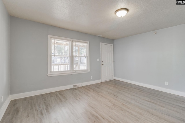 empty room with visible vents, a textured ceiling, baseboards, and wood finished floors