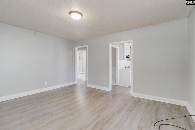 spare room with light wood-type flooring, baseboards, and a textured ceiling