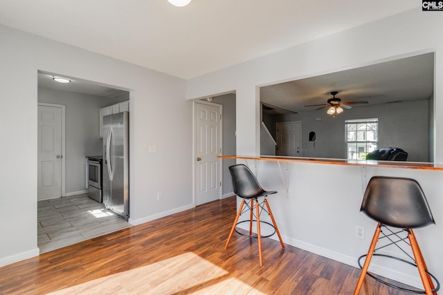 kitchen featuring appliances with stainless steel finishes, a breakfast bar area, wood finished floors, and baseboards