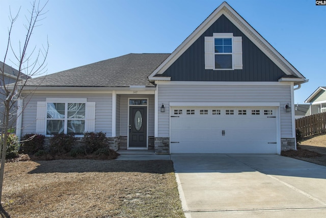 craftsman house with board and batten siding, stone siding, fence, and concrete driveway