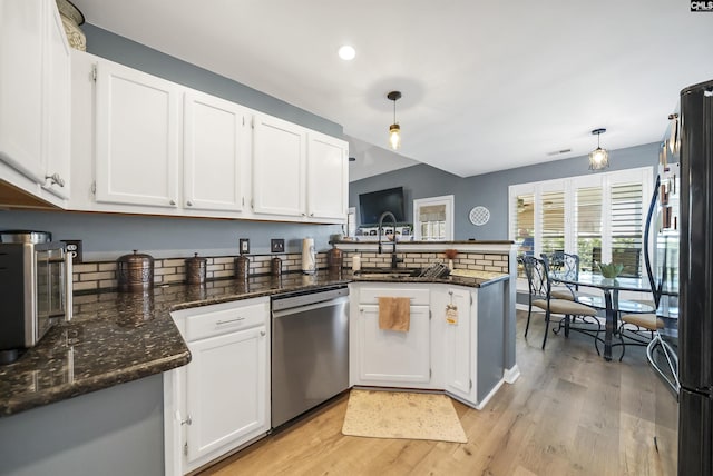 kitchen featuring a peninsula, stainless steel dishwasher, a sink, and white cabinets