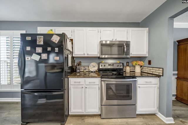 kitchen with light wood finished floors, baseboards, white cabinets, appliances with stainless steel finishes, and dark stone countertops