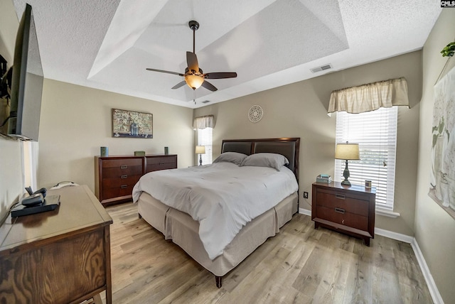 bedroom featuring a textured ceiling, visible vents, baseboards, light wood-style floors, and a raised ceiling