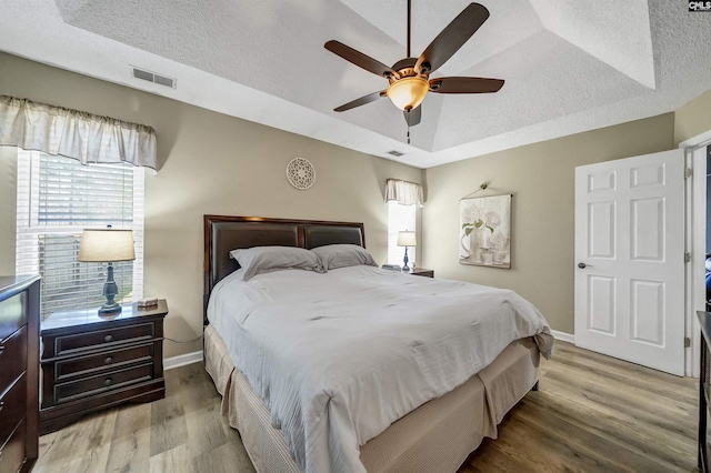 bedroom featuring baseboards, visible vents, wood finished floors, a tray ceiling, and a textured ceiling