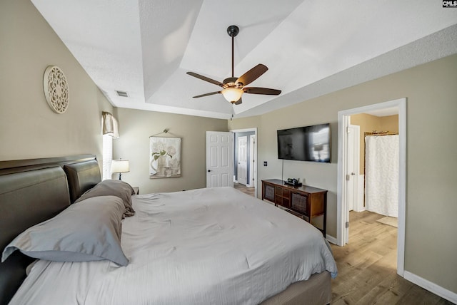 bedroom featuring baseboards, visible vents, ceiling fan, wood finished floors, and a tray ceiling