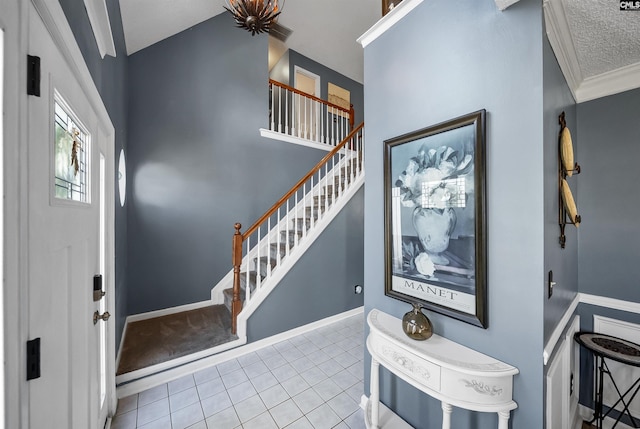 tiled foyer with stairs, ornamental molding, a textured ceiling, and baseboards