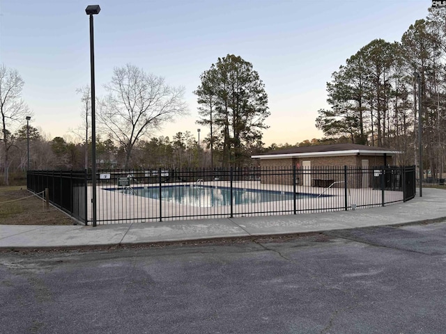 pool at dusk featuring fence and a community pool