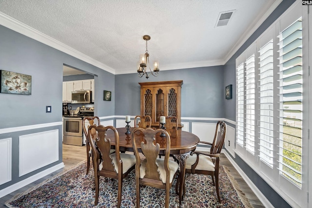 dining area featuring wood finished floors, wainscoting, visible vents, and an inviting chandelier