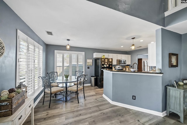 kitchen featuring baseboards, white cabinets, stainless steel microwave, freestanding refrigerator, and light wood-style floors