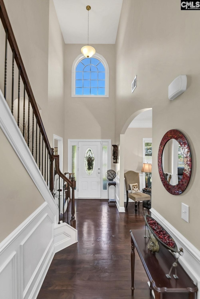 foyer entrance featuring arched walkways, wood finished floors, visible vents, baseboards, and stairs