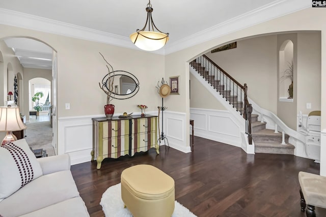 living room featuring arched walkways, a decorative wall, stairway, ornamental molding, and wood finished floors