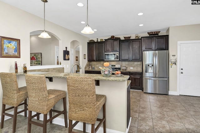 kitchen featuring pendant lighting, backsplash, appliances with stainless steel finishes, dark brown cabinets, and a kitchen breakfast bar