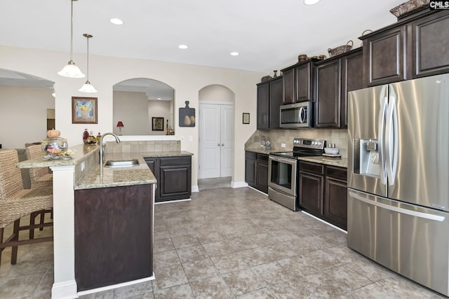 kitchen with backsplash, appliances with stainless steel finishes, a sink, a peninsula, and a kitchen breakfast bar