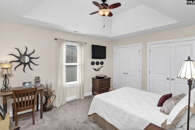 bedroom with a tray ceiling, two closets, light colored carpet, ceiling fan, and baseboards