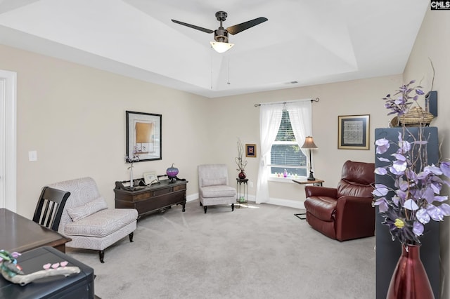 living area with carpet floors, a raised ceiling, ceiling fan, and baseboards