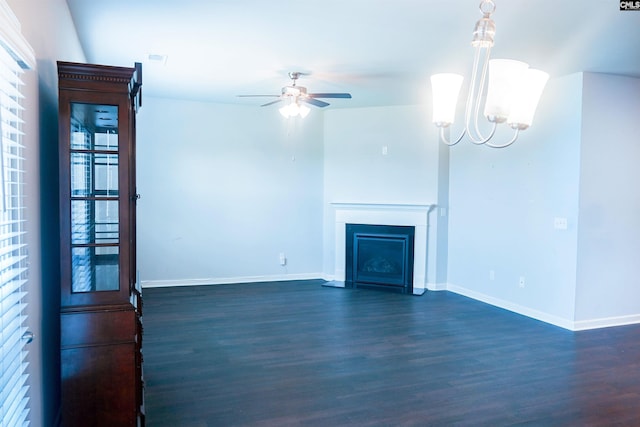 unfurnished living room featuring ceiling fan with notable chandelier, dark wood-style flooring, a fireplace, and baseboards