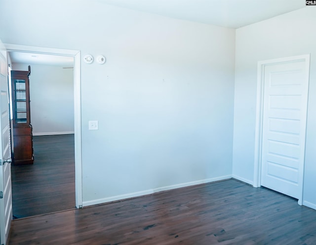 unfurnished room featuring baseboards and dark wood-type flooring