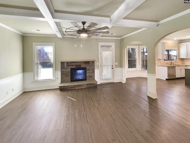 unfurnished living room with beam ceiling, a stone fireplace, dark wood-type flooring, and wainscoting