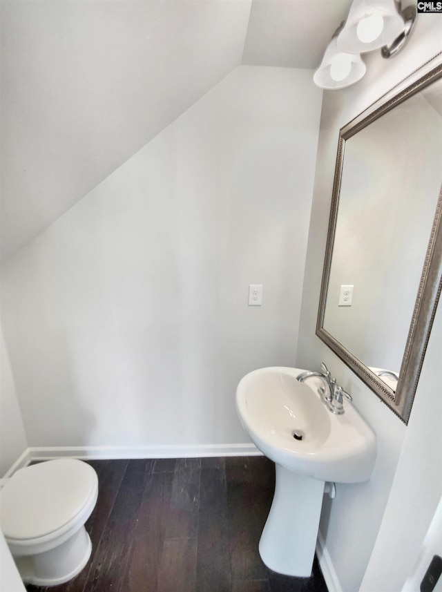 half bath with lofted ceiling, wood finished floors, toilet, and baseboards