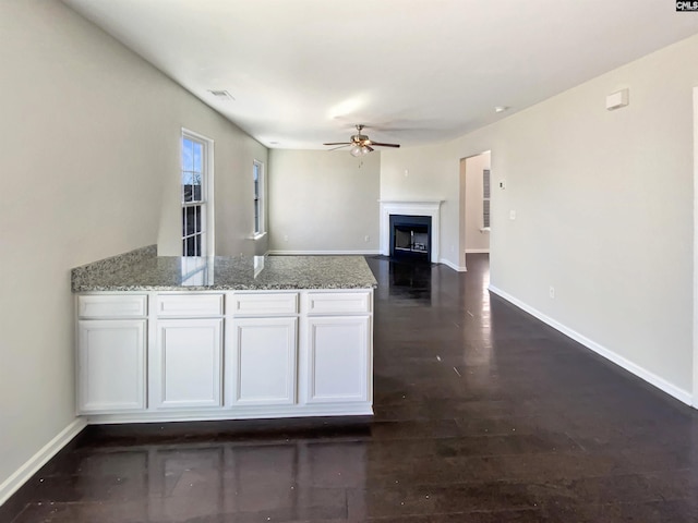 kitchen with a peninsula, light stone countertops, white cabinetry, and a ceiling fan