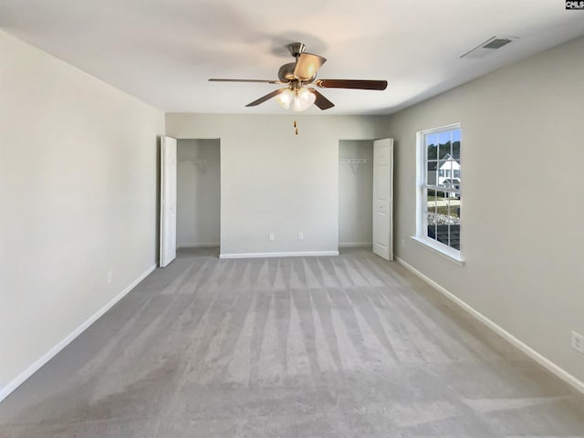 unfurnished bedroom with ceiling fan, visible vents, baseboards, carpet, and two closets