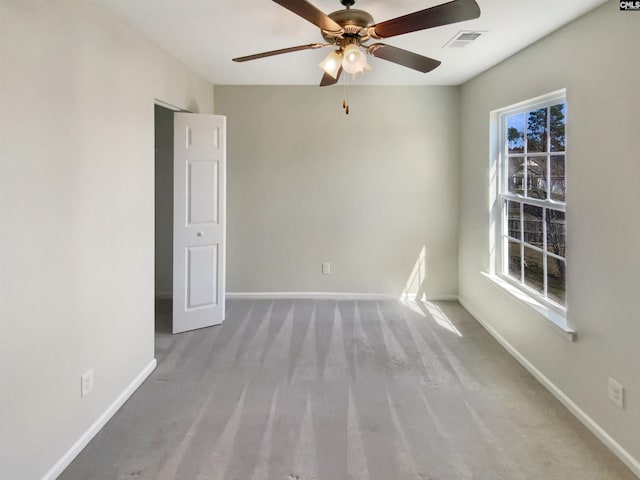 carpeted spare room featuring plenty of natural light, visible vents, ceiling fan, and baseboards