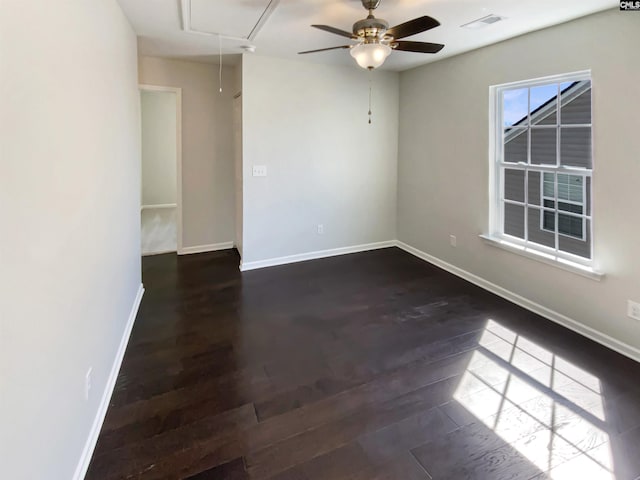 empty room with dark wood finished floors, visible vents, attic access, ceiling fan, and baseboards