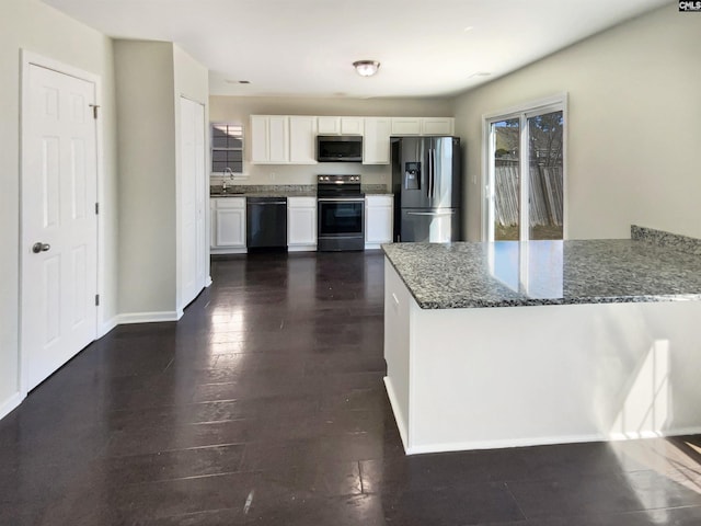 kitchen featuring dark wood finished floors, dark stone countertops, a peninsula, stainless steel appliances, and white cabinetry