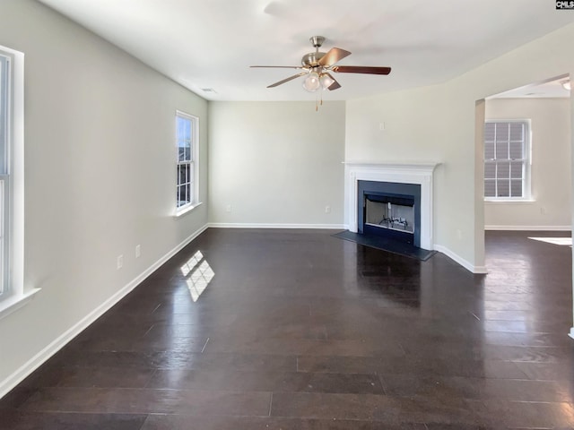 unfurnished living room with dark wood-style floors, a fireplace with flush hearth, a ceiling fan, and baseboards